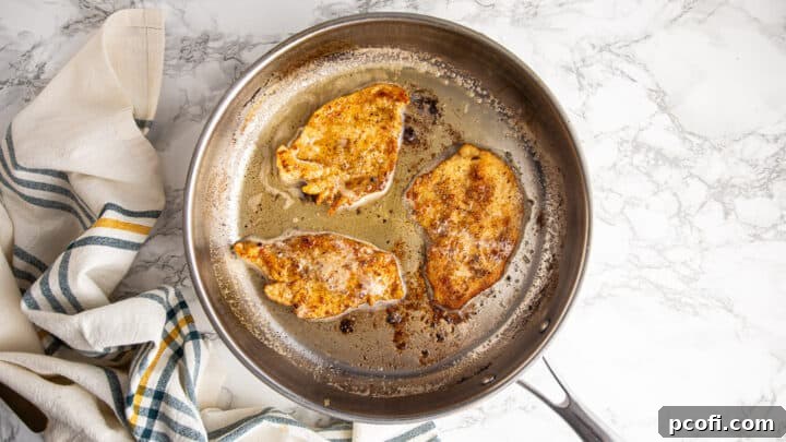 Perfectly browned chicken cutlets resting in a skillet after searing.