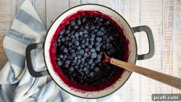 Fresh, uncooked blueberries are being added to the cooled, cooked blueberry crisp filling.
