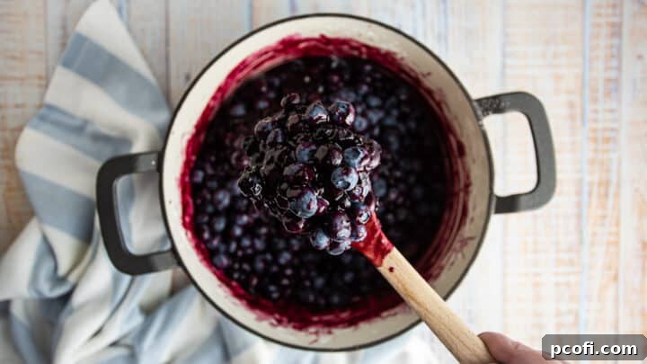 Fresh blueberries are being gently stirred into the cooked blueberry crisp filling in a pot.