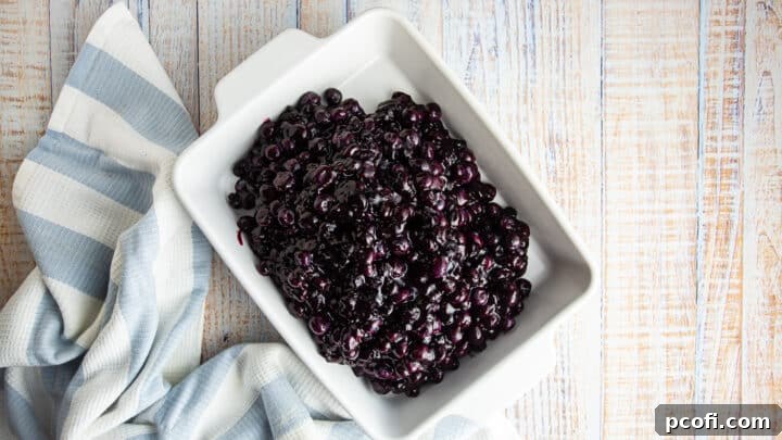 The complete blueberry crisp filling, a mix of cooked and fresh berries, is transferred into a rectangular white baking dish.