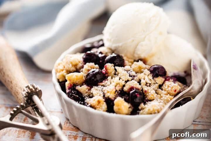 An individual serving of blueberry crumble in a small dish, with a striped kitchen towel neatly folded in the background.