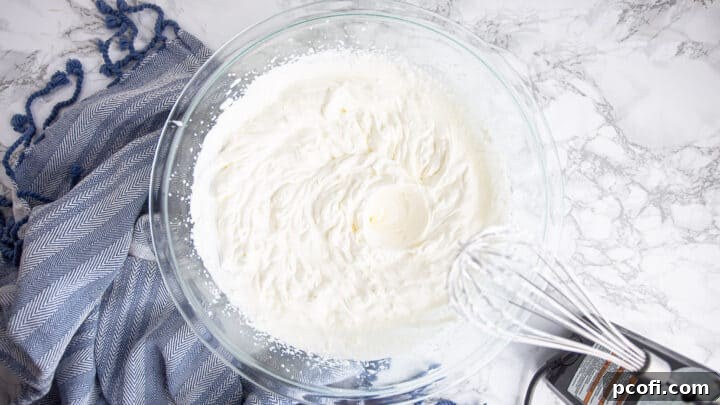 Whipping heavy cream to stiff peaks in a large mixing bowl with an electric hand mixer.
