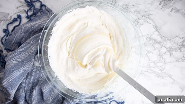 A person gently folding no-churn ice cream base ingredients together in a large bowl with a silicone spatula.
