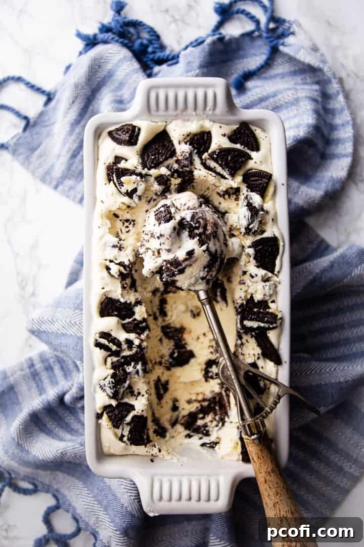 A scoop of Oreo ice cream being lifted from a loaf pan, with a blue patterned cloth in the background, highlighting its creamy texture.