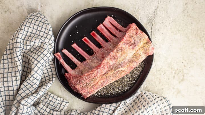 Seasoning a rack of lamb with a generous sprinkle of salt, pepper, and garlic powder.