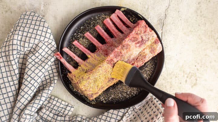 Carefully brushing a rack of lamb with a thin, even layer of tangy Dijon mustard.