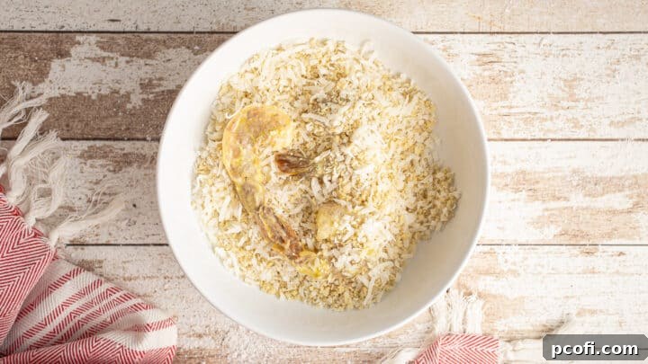 A shrimp being coated thoroughly in the coconut and breadcrumb mixture.