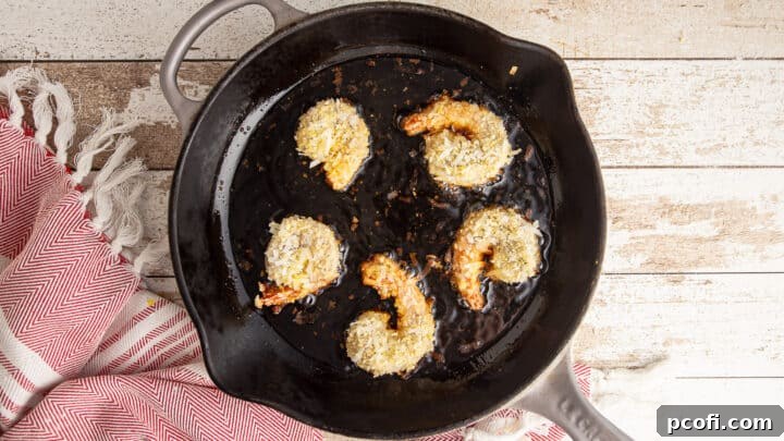 Coconut shrimp being lightly fried in a cast iron skillet until golden brown.
