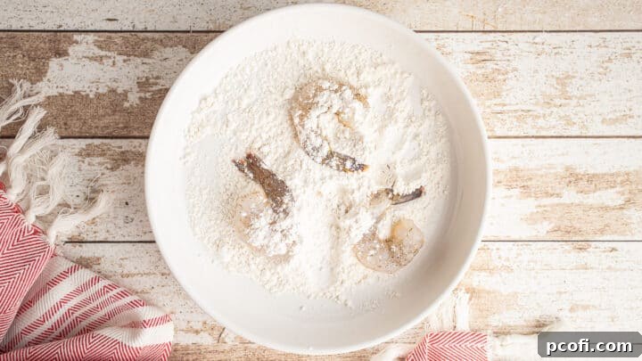 A cook lightly dusting shrimp in flour as part of the breading process.