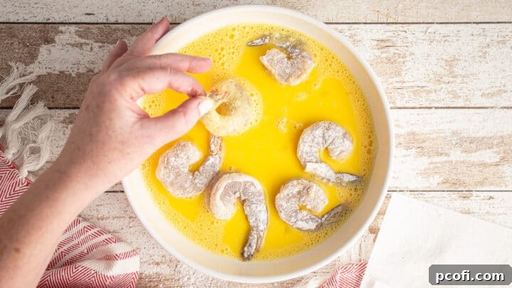 A floured shrimp being dipped into a bowl of beaten egg wash.