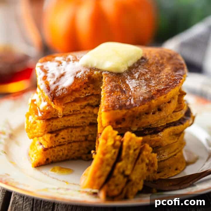 Pumpkin pancakes stacked on a vintage plate with butter and syrup.