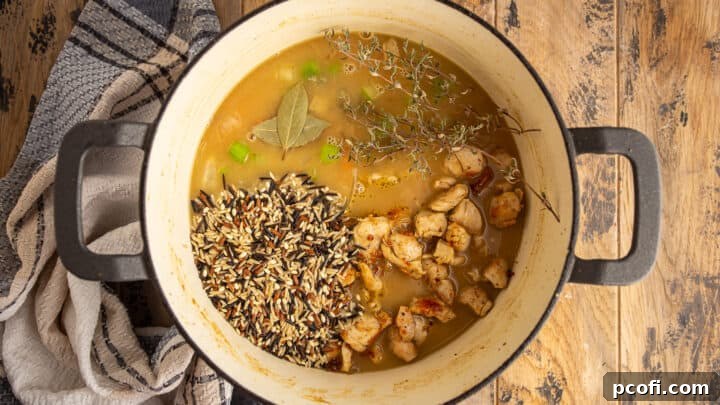 Adding cooked chicken, wild rice, and herbs to soup pot.