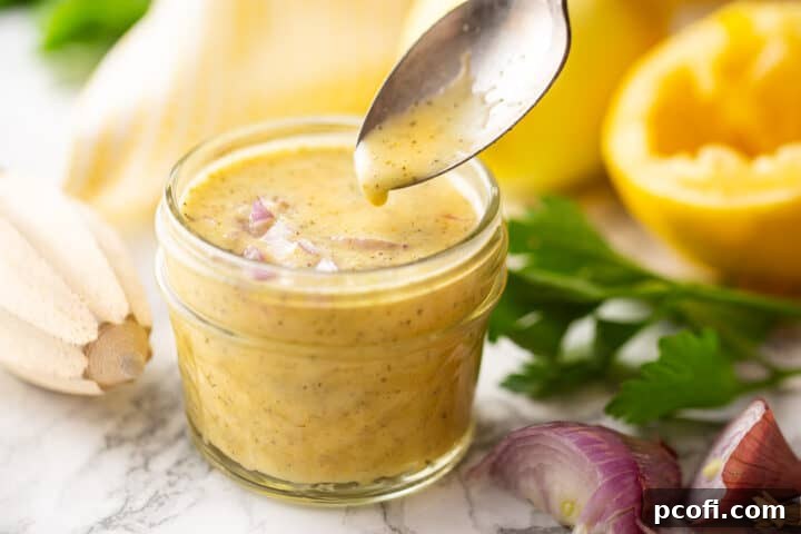 Dipping out a spoonful of lemon vinaigrette dressing recipe from a small glass jar.