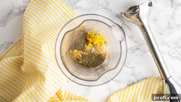 Honey, lemon zest, Dijon mustard, and seasonings gathered in the cup of a hand blender, ready for mixing.