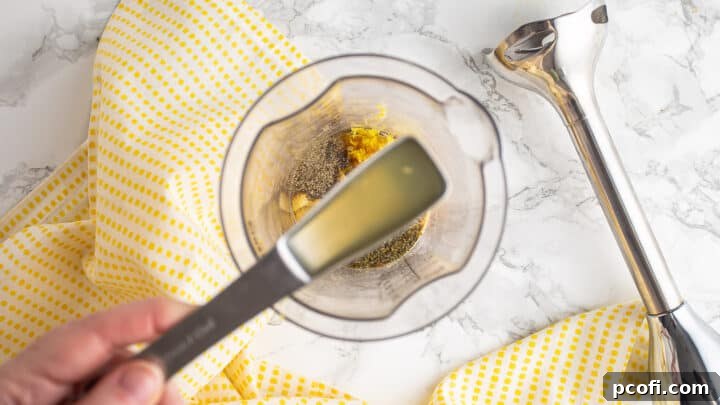 Adding fresh lemon juice to a bowl containing honey, Dijon mustard, and various seasonings, preparing for emulsification.