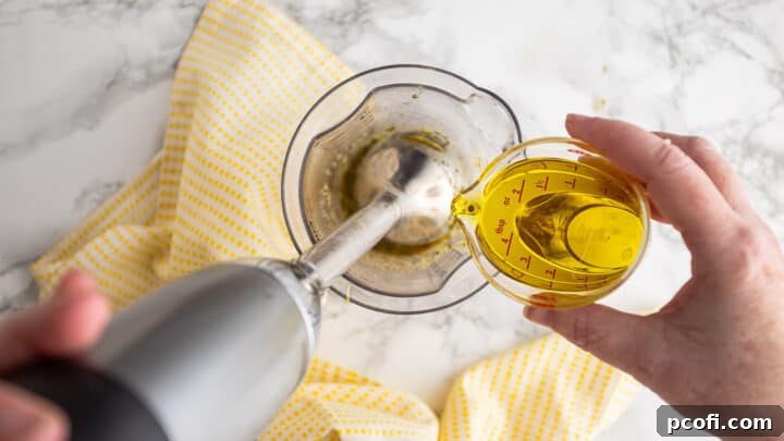 Slowly blending olive oil into the lemon juice and seasoning mixture using a whisk, demonstrating the emulsification process.