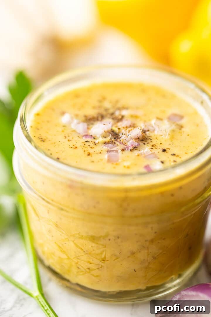 Lemon vinaigrette dressing in a quilted glass jar with freshly ground black pepper on top, ready to be served.