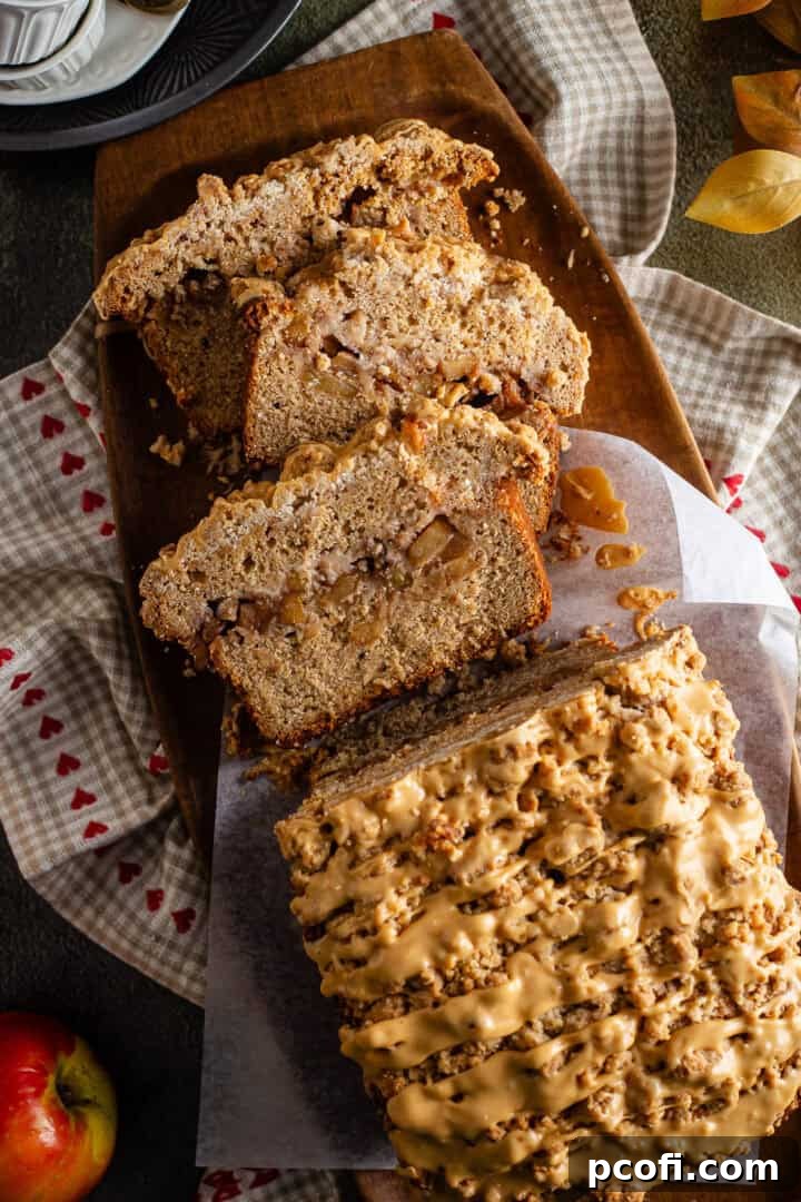 A beautifully sliced loaf of cinnamon apple bread, showcasing layers of juicy apples, a golden crumb topping, and a delicate salted caramel icing.