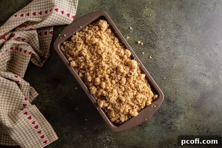 An unbaked loaf of apple bread, crowned with a generous layer of cinnamon crumb topping, ready to be placed in the oven.