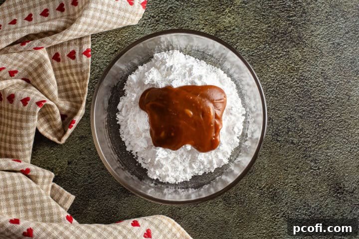A small bowl containing powdered sugar and rich caramel sauce, poised for mixing into a smooth icing.