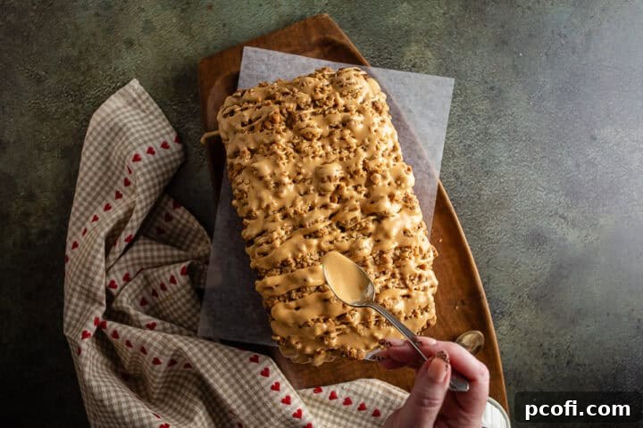 The delectable act of drizzling smooth, golden icing over a freshly baked loaf of apple bread, enhancing its visual appeal and flavor.