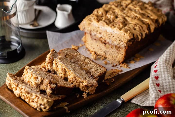 A freshly baked loaf of homemade apple bread, beautifully sliced and arranged on a rustic wooden tray, with whole apples artfully placed in the foreground.