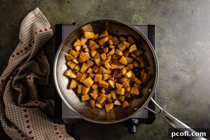 Cooked apple filling, glistening with a sweet glaze, resting in a stainless steel skillet after being gently softened.