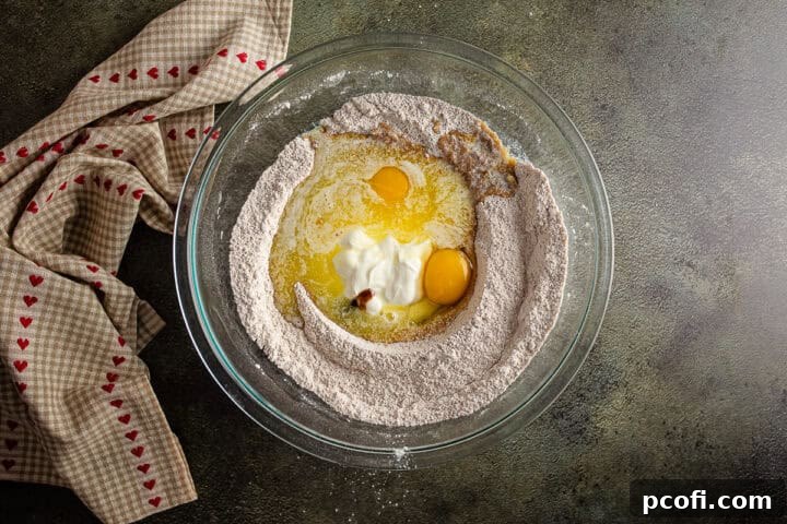 Adding liquid ingredients—sour cream, melted butter, eggs, and vanilla—into a created well in the dry ingredients for the apple bread batter.