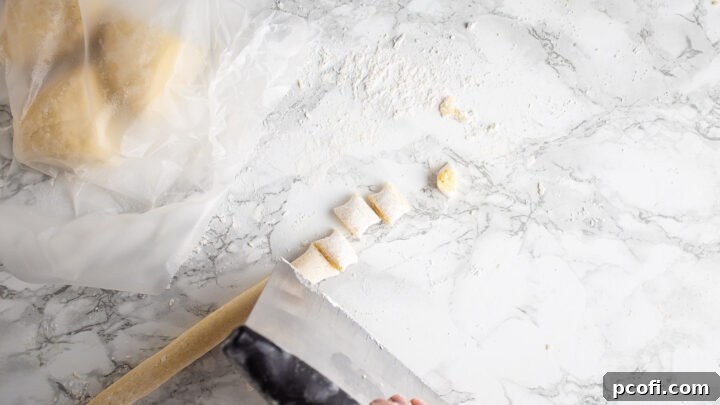 Cutting long gnocchi dough ropes into individual, uniform pillow-shaped dumplings on a wooden board.