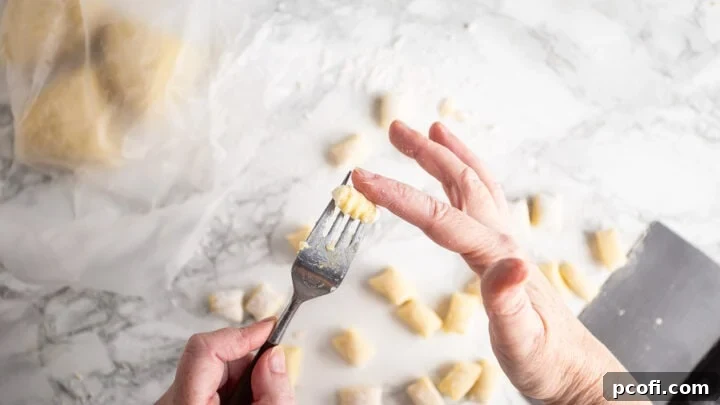 Shaping individual gnocchi by rolling them gently over the tines of a fork to create sauce-grabbing ridges, a traditional finishing touch.