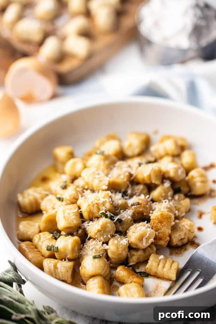 Close-up of fluffy potato gnocchi served in a pan, coated in a luscious sage brown butter sauce and topped with grated Parmesan cheese, ready to be enjoyed.