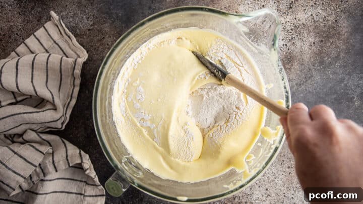 Carefully folding sifted flour into the delicate Genoise cake batter with a silicone spatula.