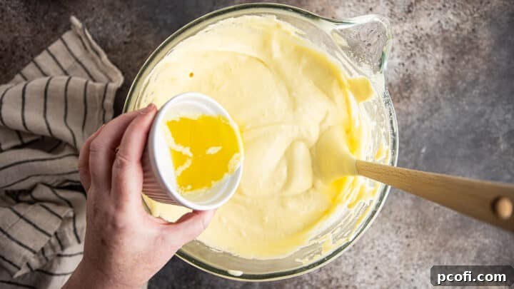 Gently incorporating melted butter into the Genoise cake batter using a folding technique.