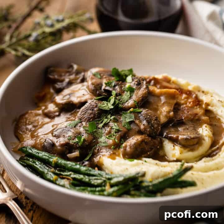 Chicken marsala served over mashed potatoes in a shallow ceramic bowl.
