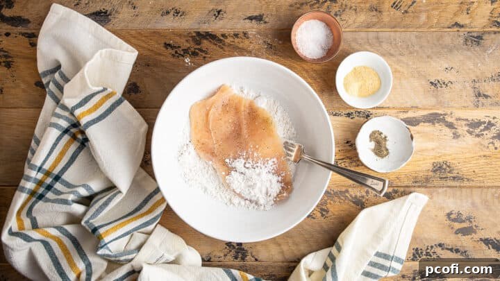 Seasoned chicken cutlets being coated in flour.