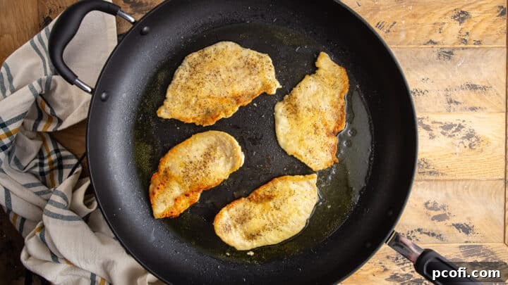 Seasoned, flour-dusted chicken cutlets sauteeing in olive oil.