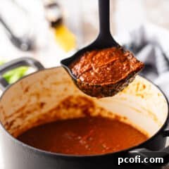 Tomato sauce being ladled from a large enameled cast iron Dutch oven.