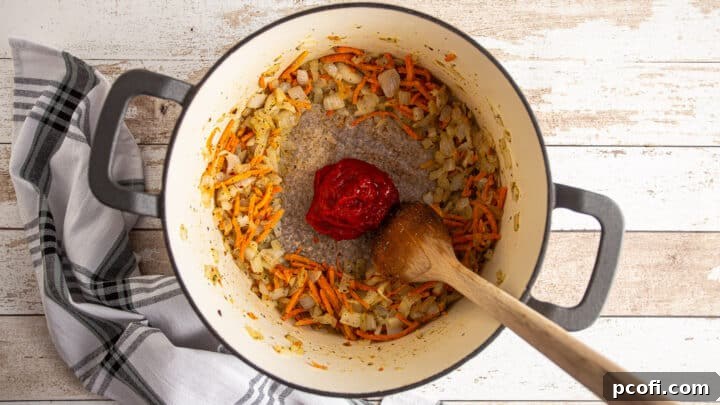 Adding tomato paste to a large pot with vegetables and seasonings.