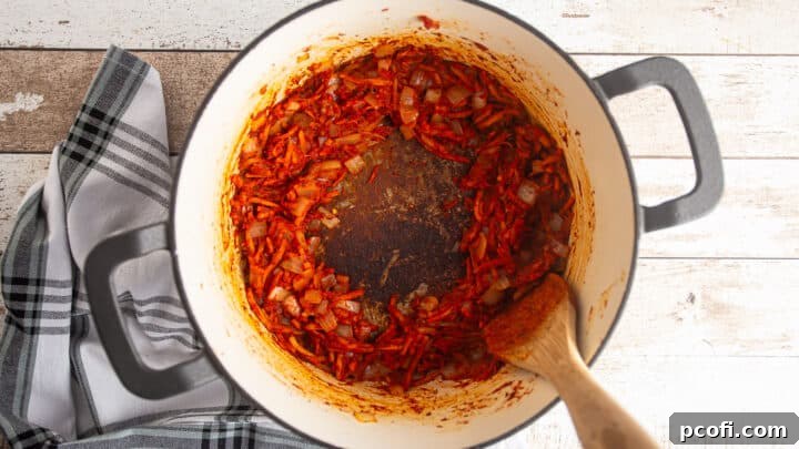 Browning tomato paste in a large pot with vegetables and seasonings.