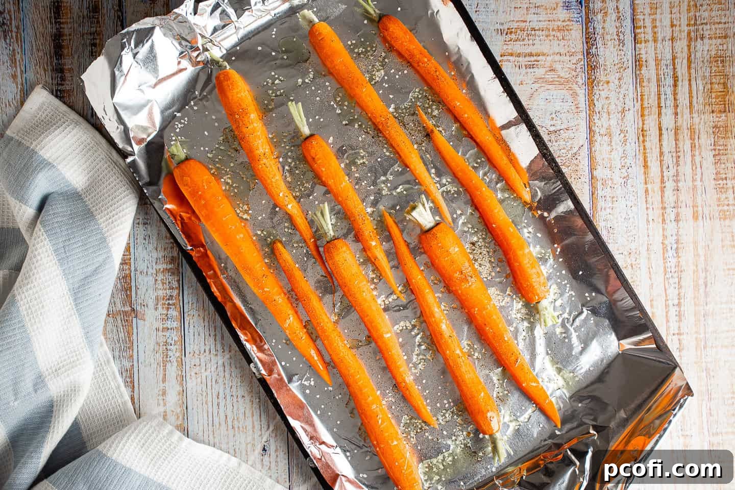 Raw carrots drizzled with olive oil and seasoned with salt and pepper, on a foil-lined sheet tray before roasting.
