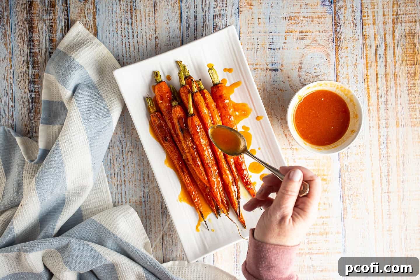 Drizzling a sweet and spicy orange sriracha glaze over roasted carrots on a platter.