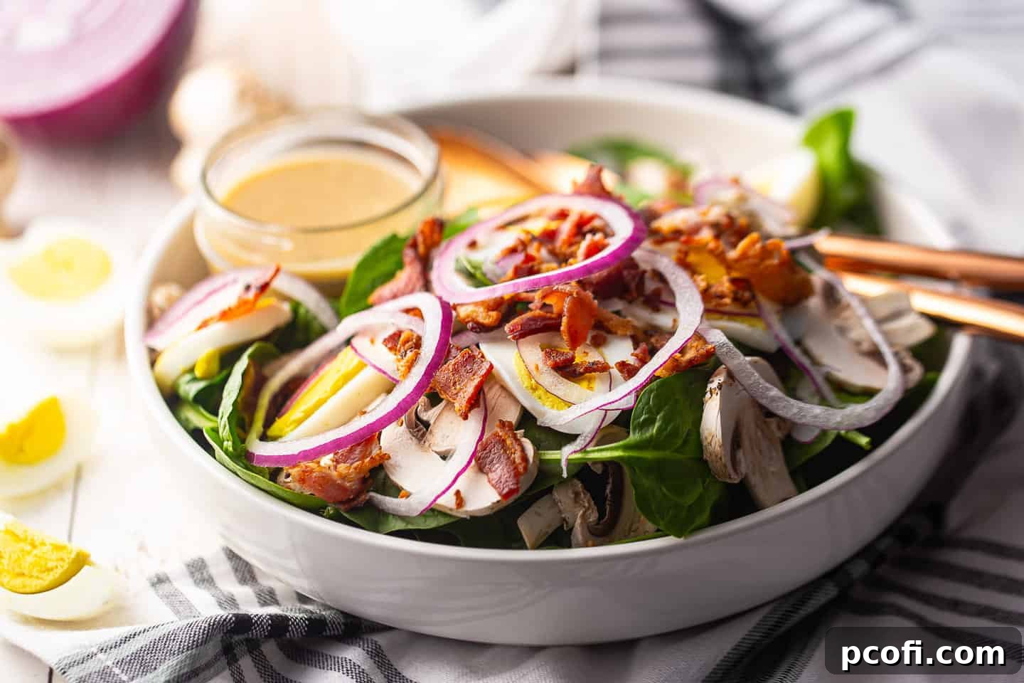 A vibrant spinach bacon salad with fresh mushrooms, hard-boiled eggs, and sweet red onion, ready to be enjoyed.