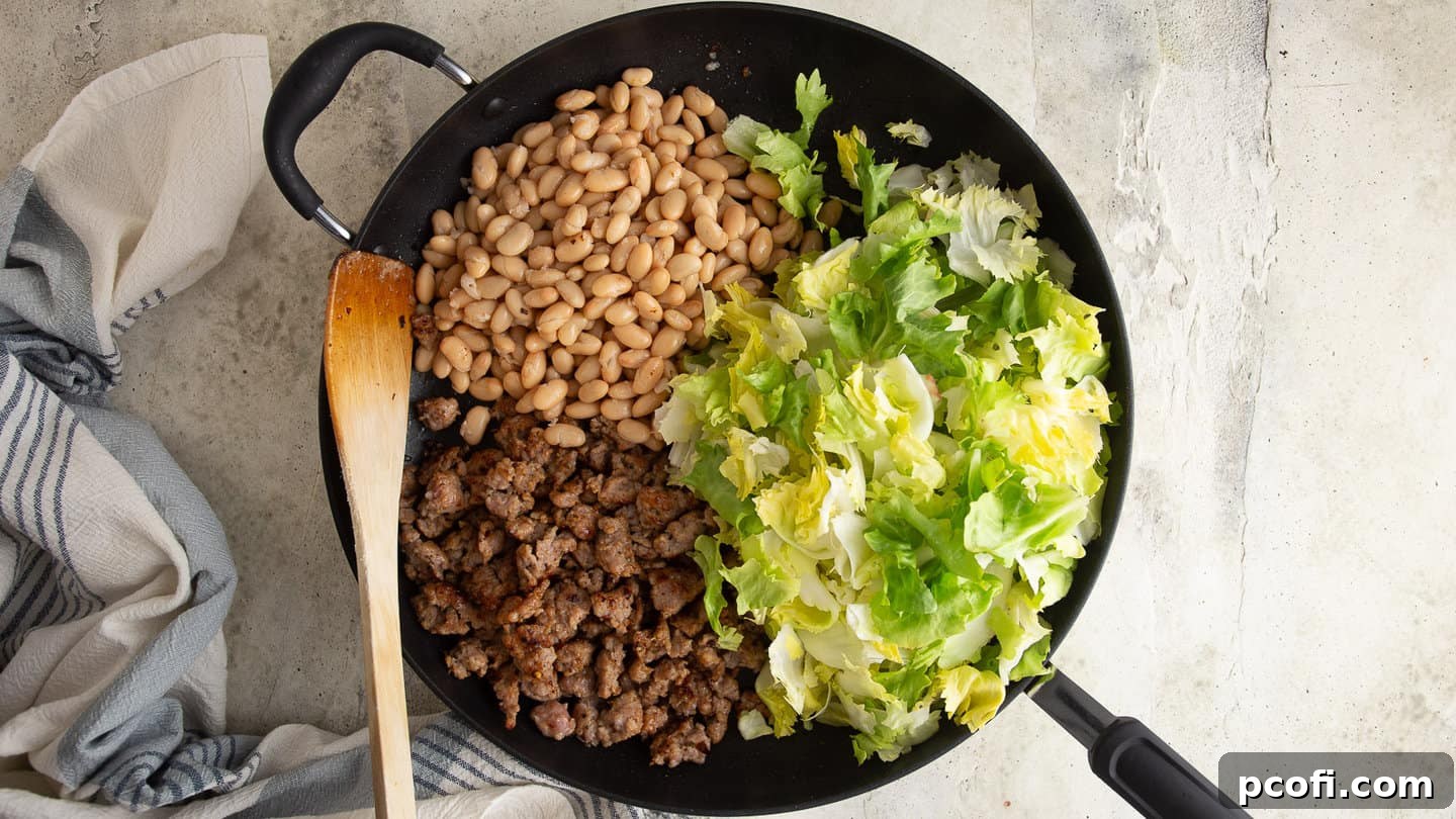 Crumbled Italian sausage, fresh escarole, and white beans combined in a large skillet, ready to be heated through.