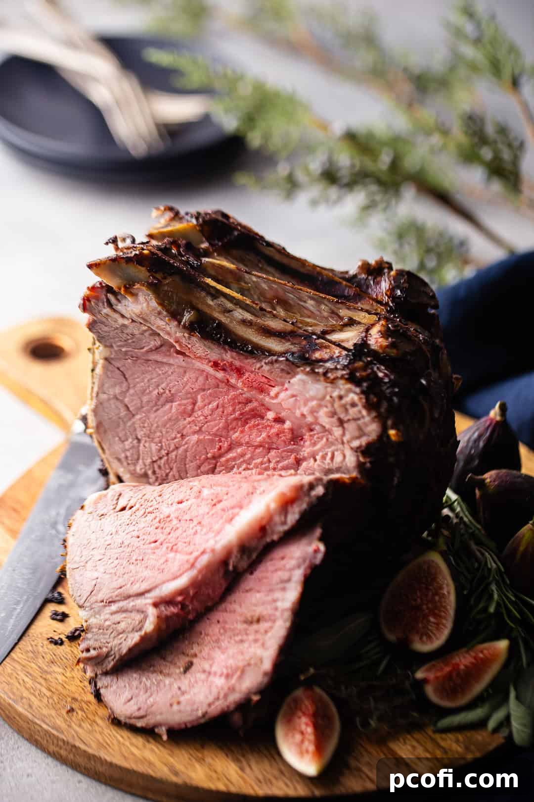 A perfectly cooked standing rib roast with several juicy slices carved and presented on a rustic cutting board, adorned with fresh figs.