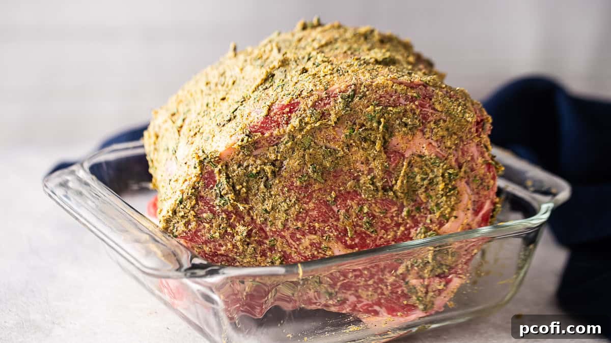 The standing rib roast is fully coated with the herbed compound butter, glistening and ready for roasting, showcasing a rich, even layer.