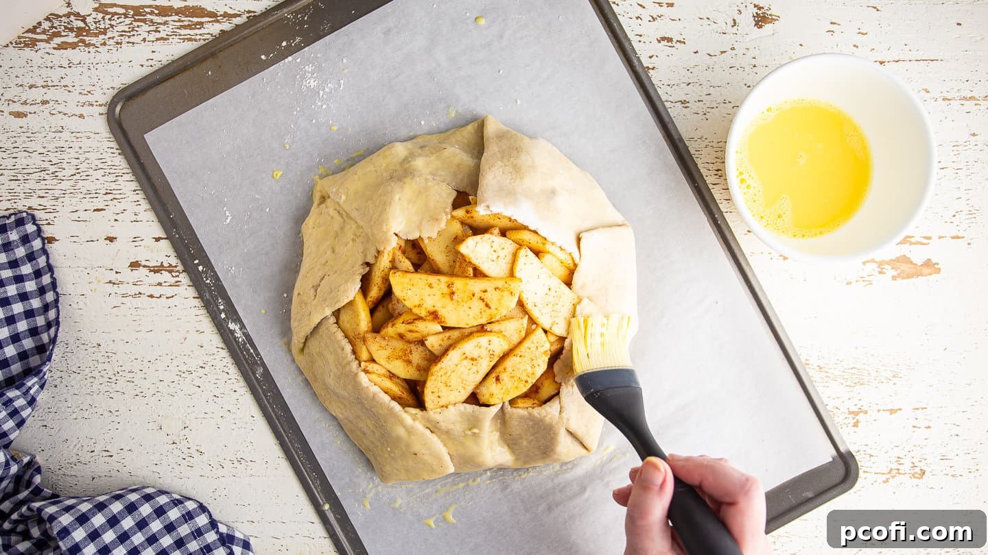 Brushing an unbaked apple galette with egg wash, preparing it for a golden, glossy finish.