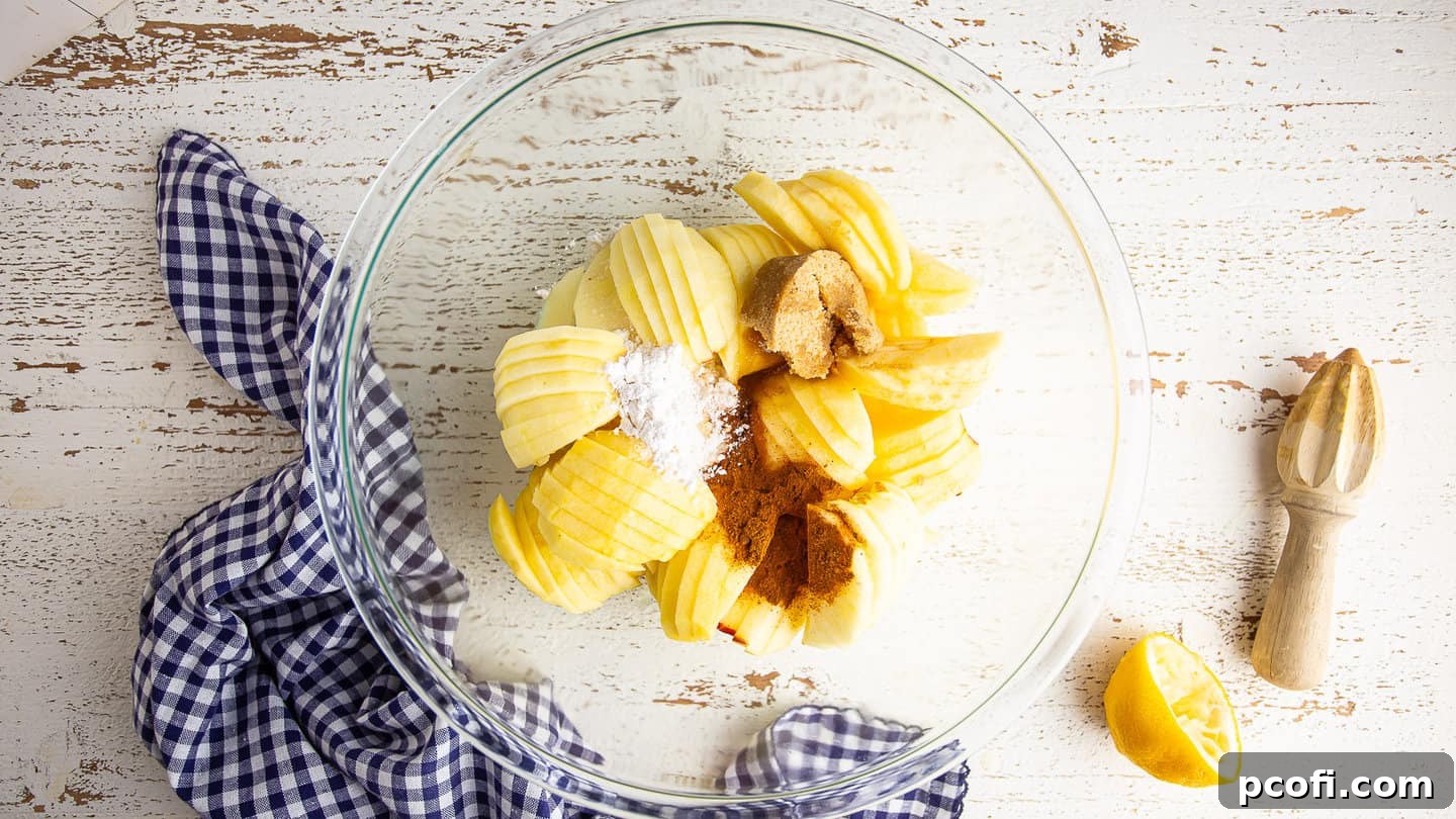 Fresh apple galette filling ingredients, including sliced apples, sugar, and spices, mixed in a large glass bowl.