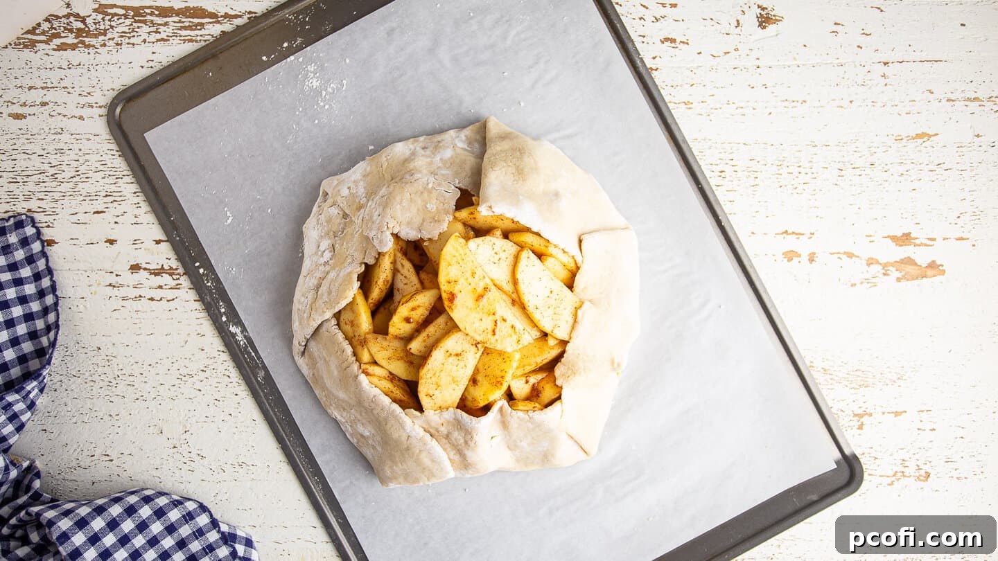 Unbaked apple galette, beautifully formed with rustic edges, resting on a parchment-lined baking sheet.