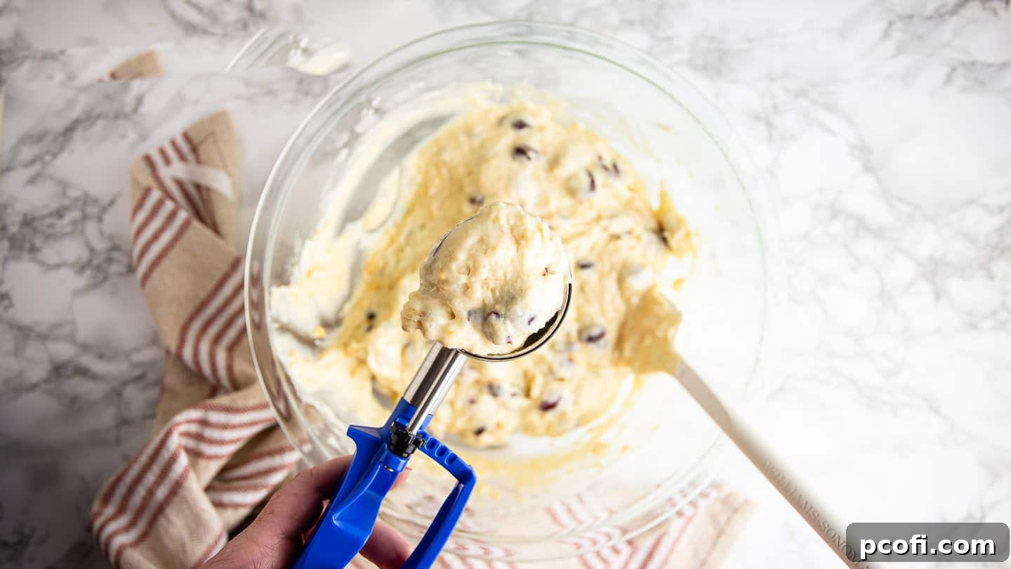 Muffin batter being scooped into a muffin tin using a trigger scoop, ensuring uniform portions.