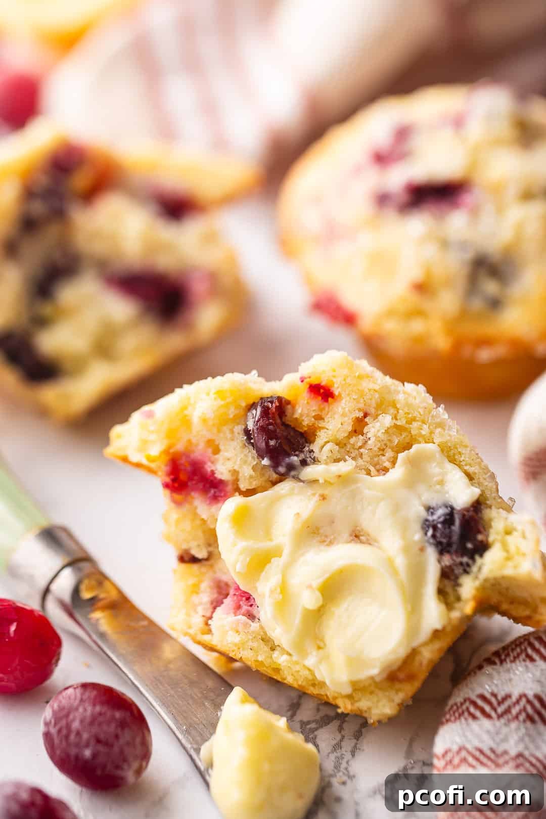 A freshly baked cranberry orange muffin, split open and generously buttered, showcasing its moist, tender interior.
